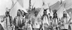 A group of Spokane Indians standing in front of their tipis in traditional garments