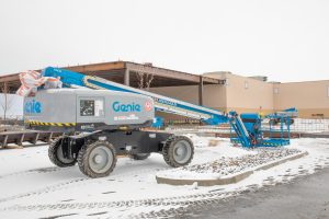Genie cherry picker sitting in snow by the new administration building expansion