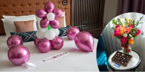 Birthday setup on a bed with a pink balloon bouquet and a ‘Happy Birthday’ sash; inset shows a colorful flower bouquet and chocolates on a round table.