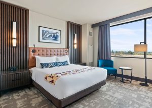 Hotel room with a king bed, tufted headboard, two nightstands, wall lamps, and abstract art above the bed.