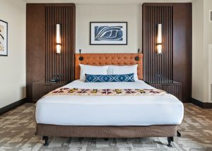 King bed with tufted orange headboard, dark wood panels, two nightstands, wall sconces, and framed abstract art above the headboard.