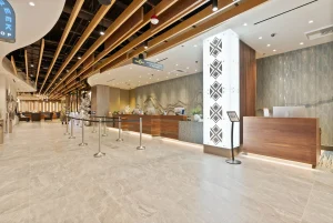 Modern hotel lobby with exposed wooden ceiling beams, a long reception desk, and rope barriers guiding guests.