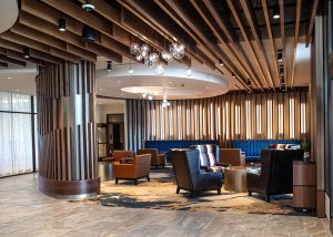 Hotel lobby lounge with brown leather chairs, blue banquette seating, wooden slat walls, and glass globe pendant lights.