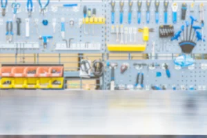 Blurred view of a tool-filled workshop pegboard with wrenches, pliers, and yellow storage bins behind a workbench