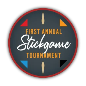Circular badge with dark blue center and red outer ring, displaying orange text 'First Annual' above a white cursive word and the word 'TOURNAMENT' in orange at the bottom.