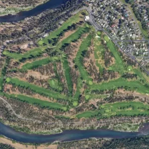 Aerial view of a winding golf course on a hillside beside a river, with a small town visible in the upper-right.