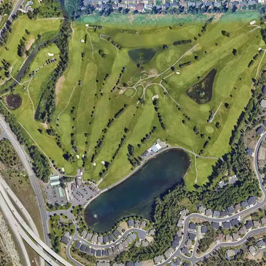 Aerial view of a golf course with multiple fairways, greens, and a large central pond surrounded by roads and houses nearby